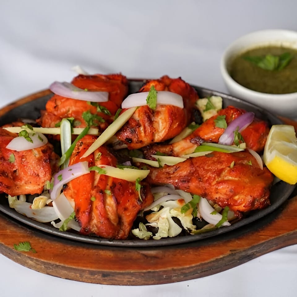 Indian Tandoori Chicken drumsticks with onions, ginger, and lemon on a sizzling platter with green chutney.