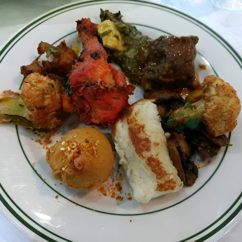 A white plate with a green rim holds a variety of Indian dishes, including tandoori chicken and curries.