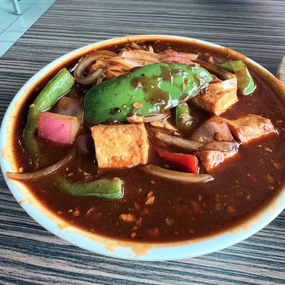 A close-up of Indian chili paneer with green peppers, onions, and tofu in a rich brown sauce.