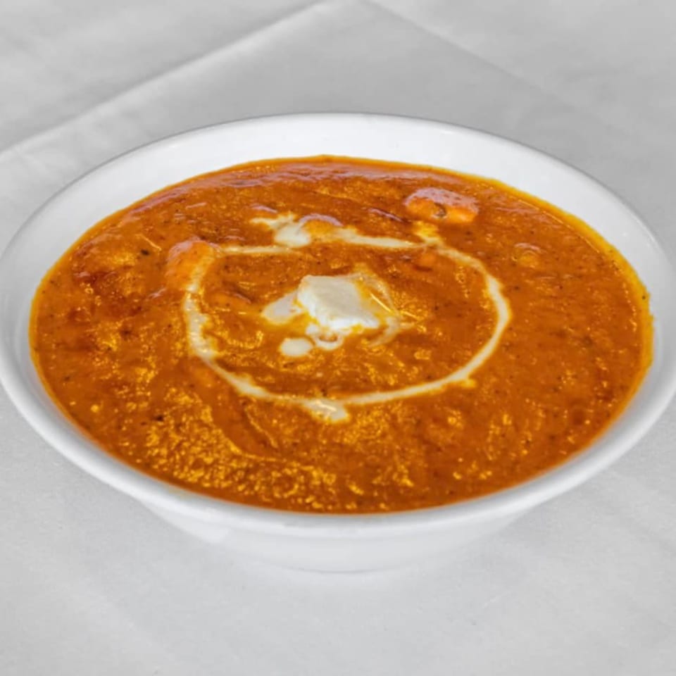 A white bowl filled with orange Indian curry, garnished with a swirl of cream.