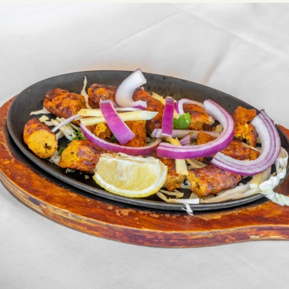 Indian chicken tikka with red onions, ginger, and a lemon wedge on a sizzling platter.