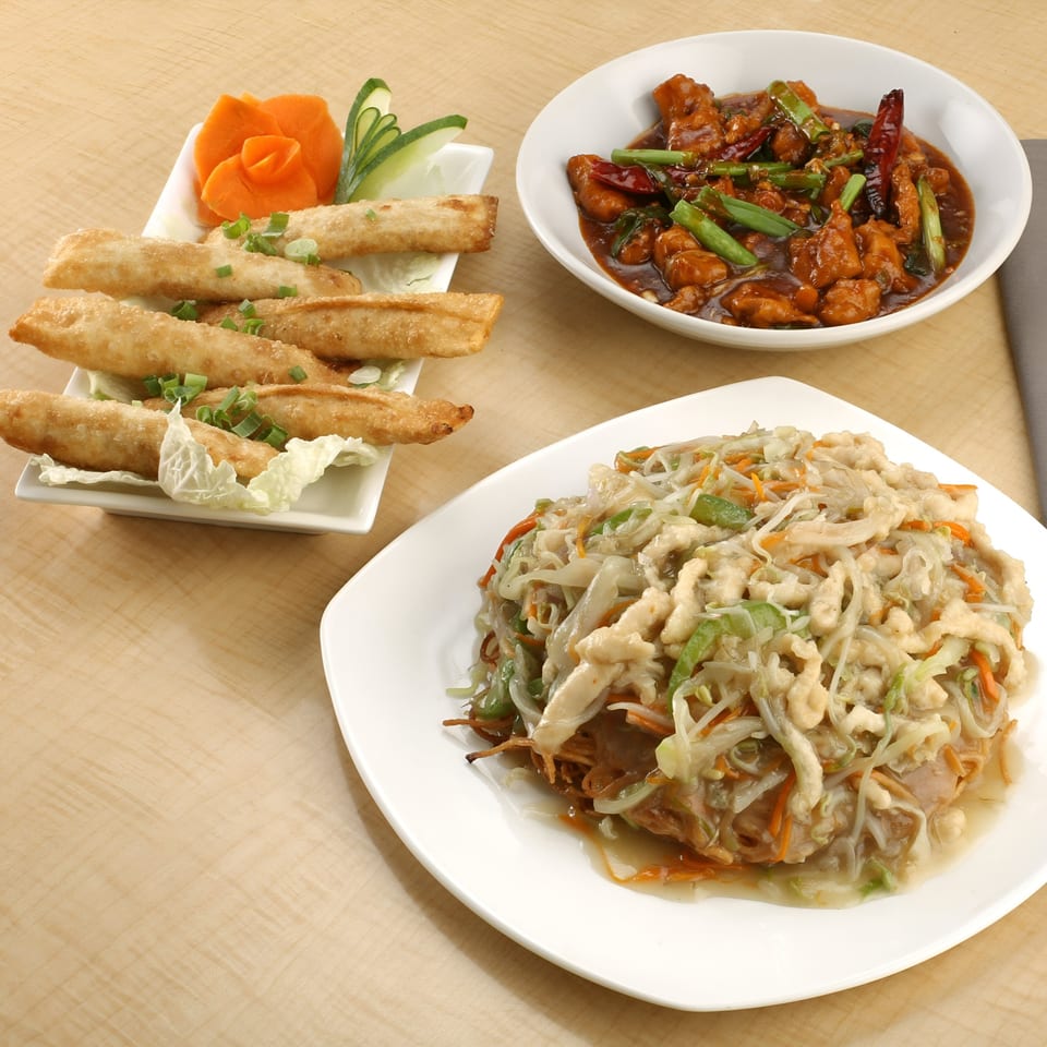Three Indian dishes: spring rolls, chili chicken, and chicken chowmein, on a light wooden table.